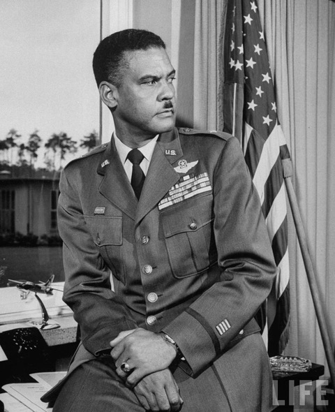Black and white image of Brigadier General Benjamin O. Davis sitting with American flag behind him